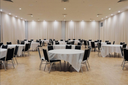 Empty banquet hall with round tables draped in white cloths and black chairs arranged for an event.