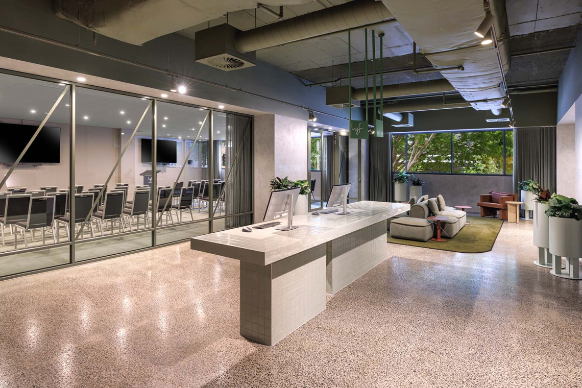 Modern lobby with a marble reception desk, glass-walled conference room to the left, and a seating area with sofas and plants.