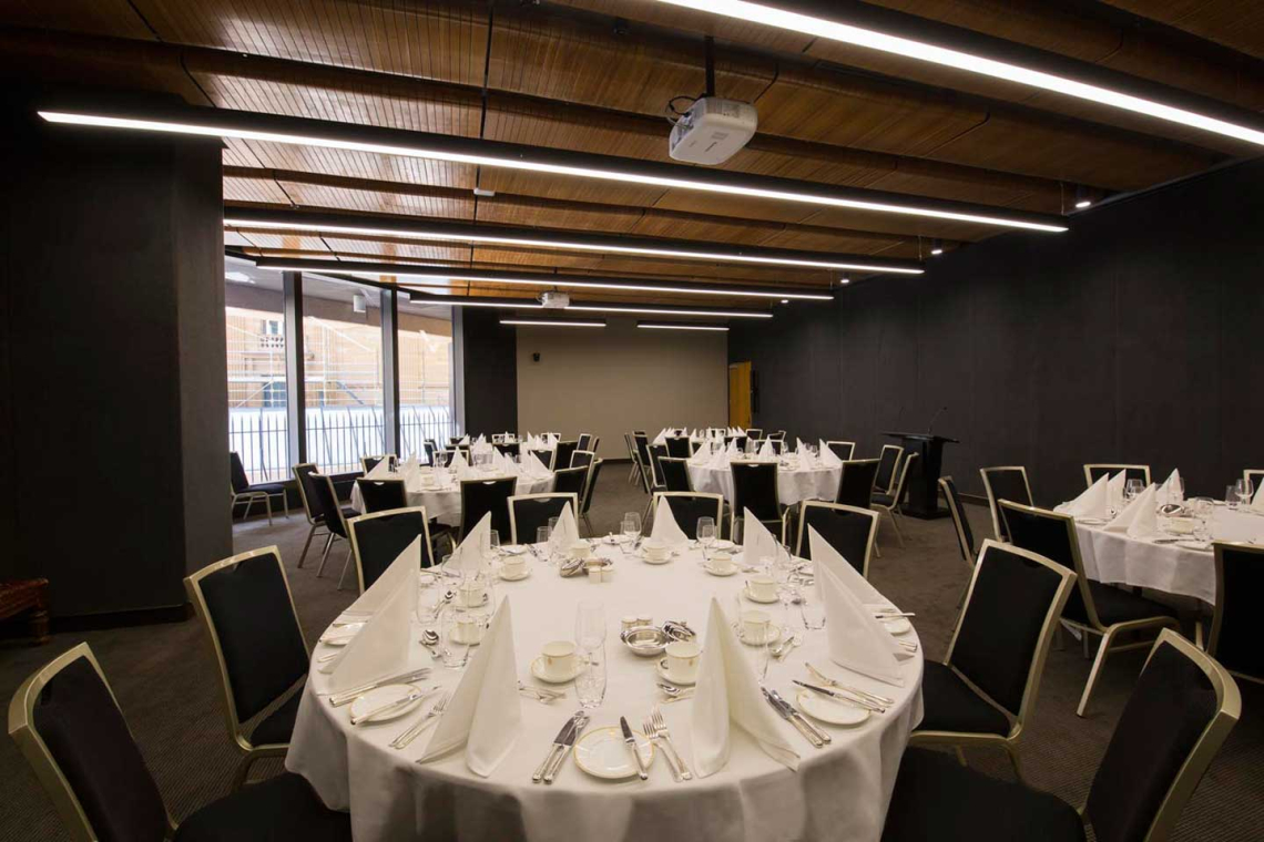 Banquet hall set with round tables covered in white linens, folded napkins, and formal place settings ready for a event.