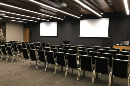 Banquet hall set for a formal dinner with round tables, white tablecloths, folded napkins, and black chairs.