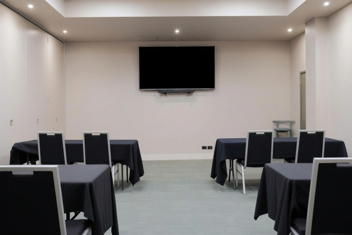 Conference room with black-tablecloth tables arranged for a presentation and a wall-mounted TV at the front.