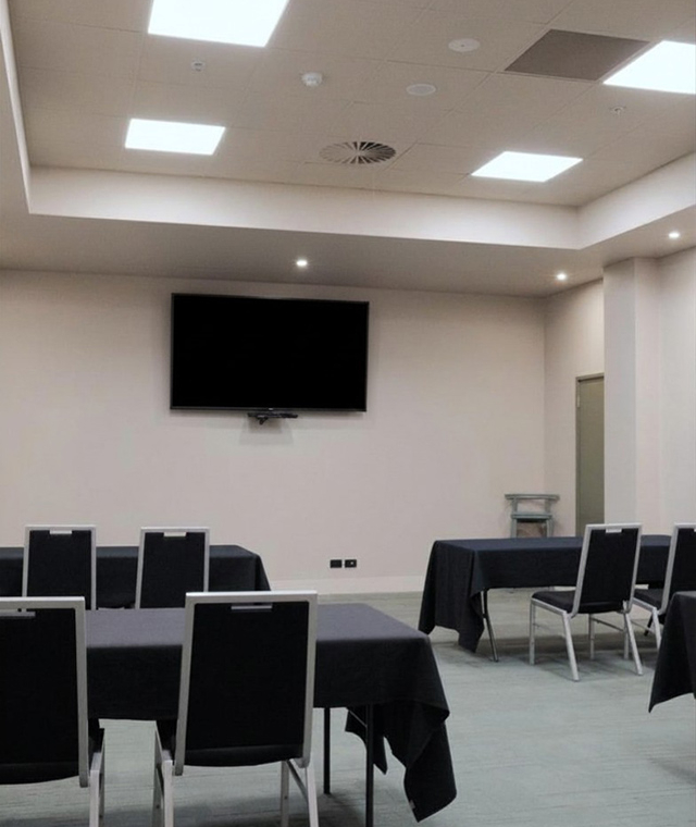 Empty conference room with tables covered in black cloths and a wall-mounted TV screen above.