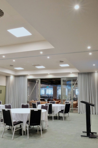 Event space set for a gathering with round tables in white cloths, black chairs, and a black podium on the right.