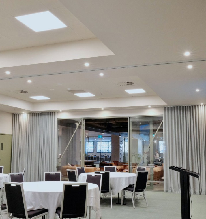 Event space set for a gathering with round tables in white cloths, black chairs, and a black podium on the right.
