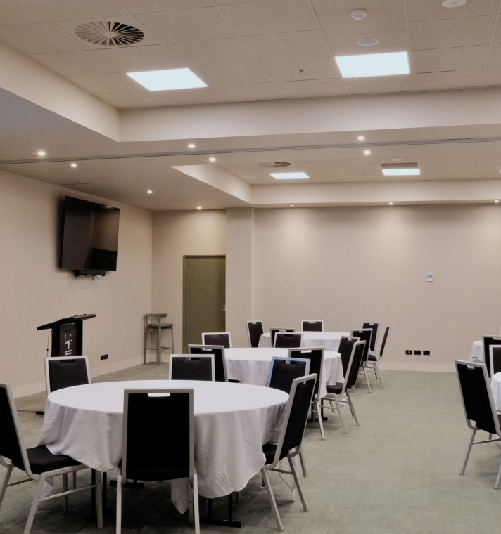 Banquet-style conference room with round tables covered in white cloths and black chairs around them.